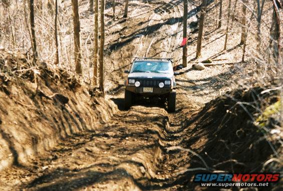 Jeep Cherokee XJ climbing a rutted dirt trail in a wooded area