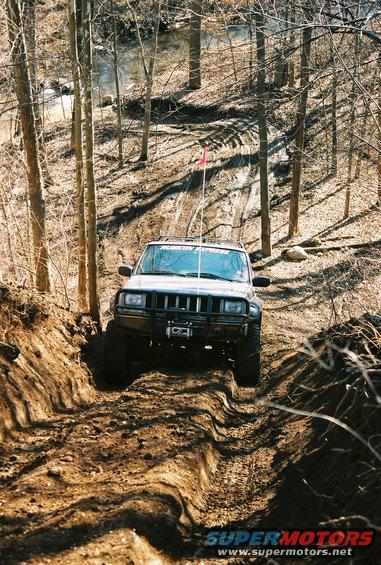 Jeep Cherokee XJ climbing a steep dirt trail with trees on either side