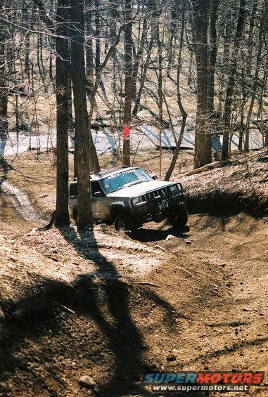 Jeep Cherokee XJ climbing a dirt hill in a wooded area