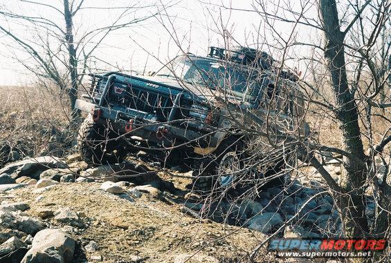 Dark Jeep Cherokee XJ with roof rack navigating rocky terrain