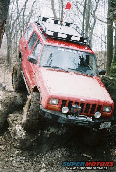 Red Jeep Cherokee with roof rack and winch navigating rocky terrain