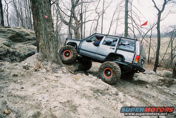 Silver Jeep Cherokee XJ with large tires climbing a rocky hill off-road