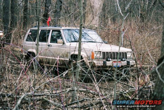 Jeep Cherokee XJ with a red flag on the roof driving through dense woods