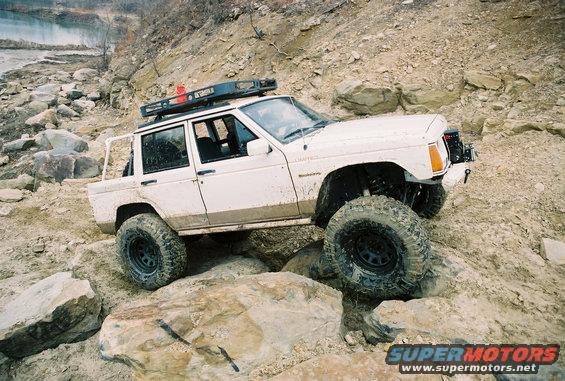 White Jeep Cherokee with roof rack navigating rocky terrain