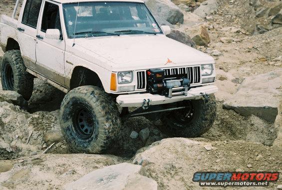White Jeep Cherokee XJ with large tires and a winch on a rocky terrain