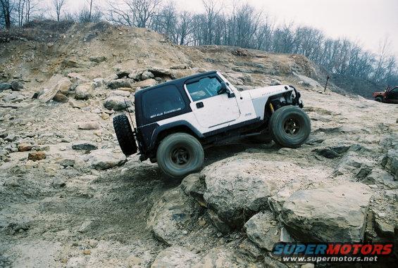 White Jeep Wrangler TJ climbing rocks, spare tire on rear