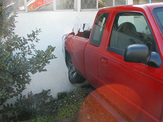 Red Ford Ranger pickup truck with its rear end embedded in a white stucco wall