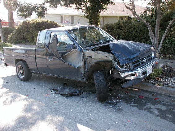Dark blue pickup truck with severe front-end damage and driver's side door ripped open, parked on a residential street