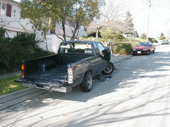 Dark gray pickup truck with damaged front end, parked on a residential street