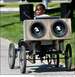 1990 Ford Bronco - A custom-built vehicle, a large speaker system, is seen from the side as it is driven by a young person.