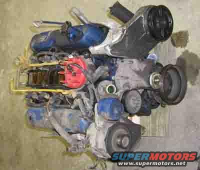 Engine with red distributor cap and blue valve covers against a concrete wall