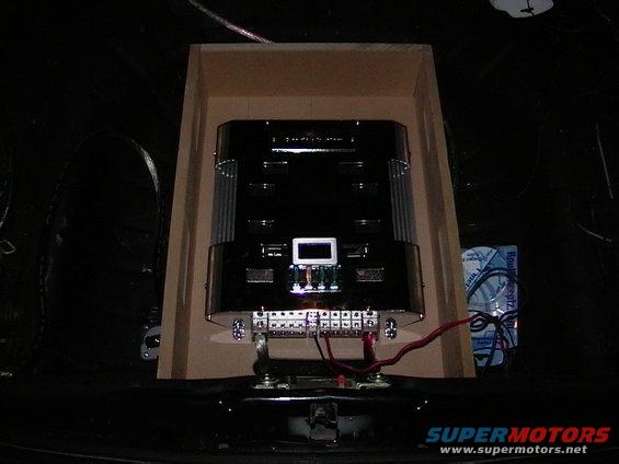Car amplifier mounted in a wooden enclosure, with wiring visible