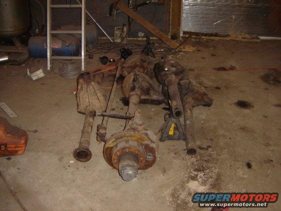 Several rusty vehicle axles and differential assemblies on a concrete floor