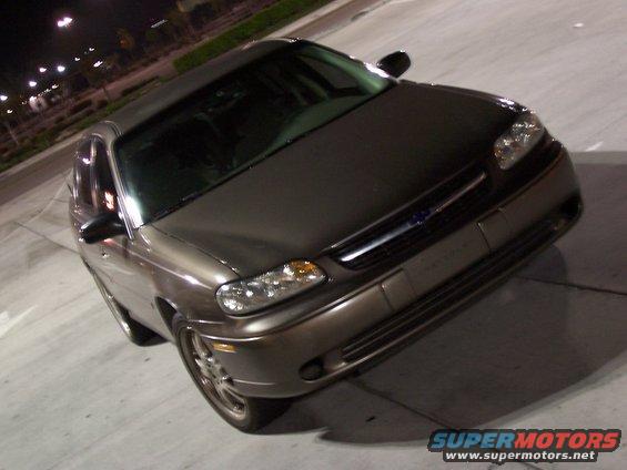 Front view of a dark gray Chevrolet Malibu parked at night. The grille has a blue bowtie emblem