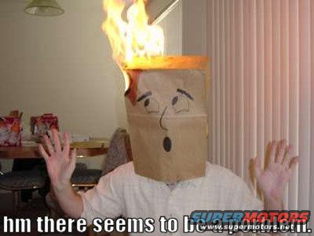 Person wearing a paper bag with a drawn face, flames erupting from the top. Hands raised in a gesture of surprise