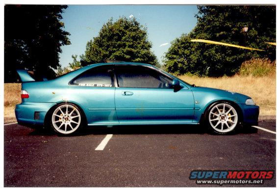 Teal coupe with white aftermarket wheels and a rear spoiler, parked on asphalt