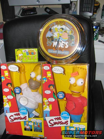 Homer and Bart Simpson action figures in boxes, a Moe's Tavern clock, and a box of cookies
