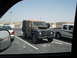 1988 Ford Bronco - A utilitarian Land Rover Defender is parked in a lot, alongside other vehicles under a clear sky.