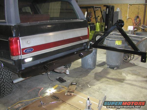 1987 Ford Bronco rear bumper with a black spare tire carrier attached. A forklift is visible in the background