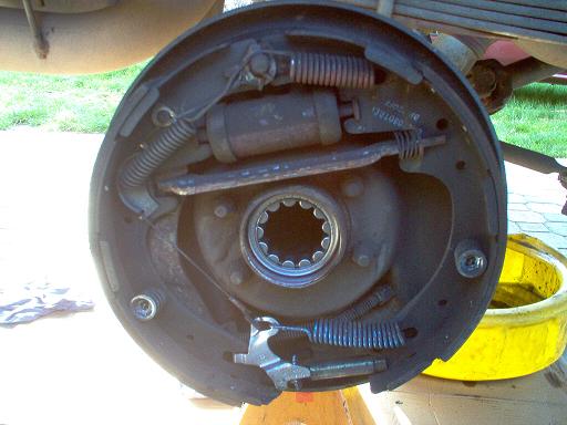 Brake drum assembly with visible springs, brake cylinder, and splined axle hub. Yellow bucket in background