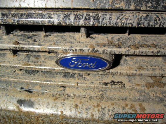Close-up of a muddy Ford emblem on a grille. Supermotors.net logo visible