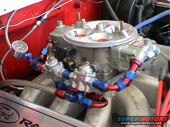 Close-up of a carburetor with fuel lines and a pressure gauge attached