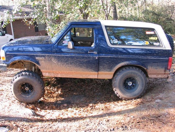 1995 Ford Bronco side profile, blue with white top, lifted with large off-road tires, covered in mud
