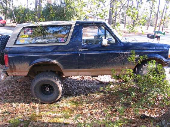 Dark blue Ford Bronco with tan top, spare tire on back, covered in mud. Has JEGS sticker on window