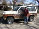 1986 Ford Bronco II - A boy stands next to a white and brown 1986 Ford Bronco II with visible rust and aftermarket wheels.