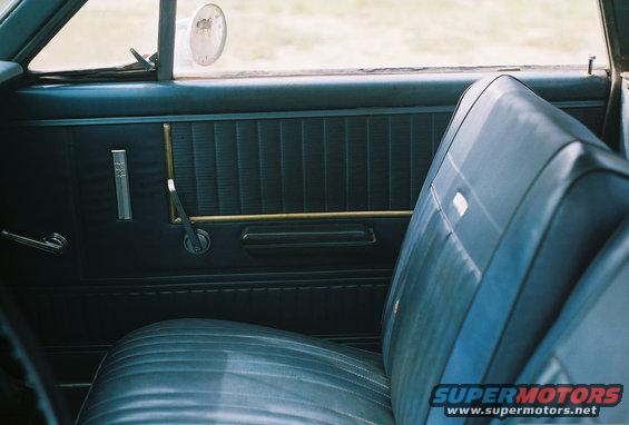 Blue vinyl interior door panel with chrome handle and window crank, and part of a blue seat