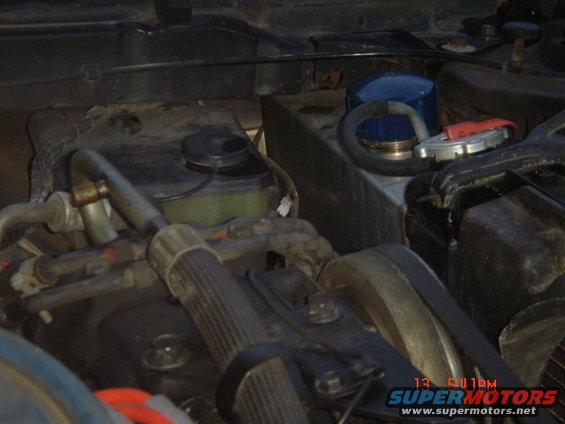 Tank on shelf in front left corner of engine compartment.