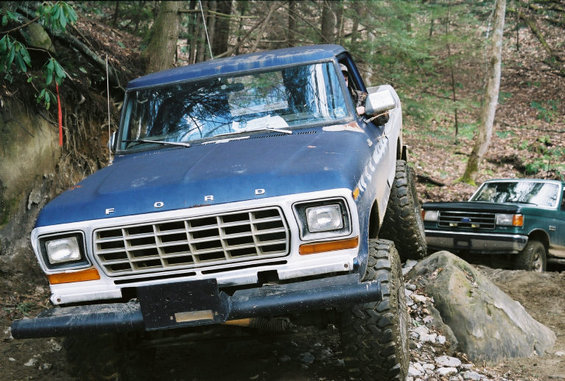 Blue Ford F-150 truck with off-road tires on a rocky trail, another green truck behind it