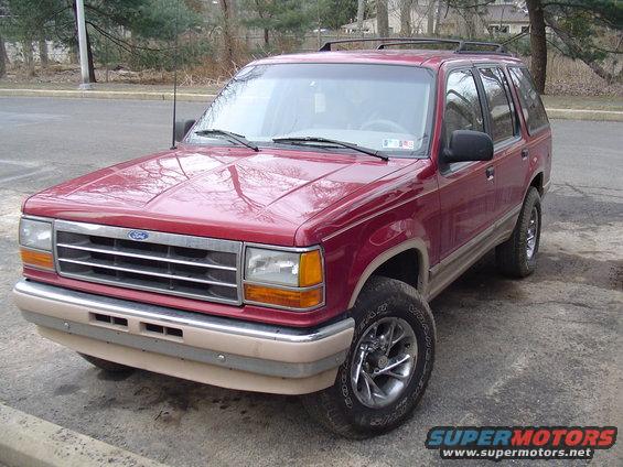1992 Ford Explorer parked on asphalt, front 3/4 view. Red paint, tan lower body trim, roof rack