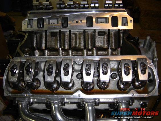 Close-up of a V8 engine's cylinder heads and intake manifold, showing rocker arms and exhaust headers