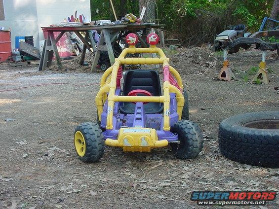Purple and yellow toy dune buggy with red steering wheel, sitting in a dirt yard