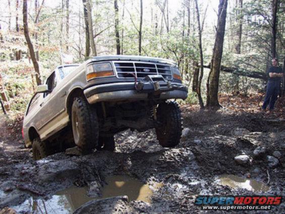 1995 Ford Bronco navigating a muddy trail with one wheel lifted