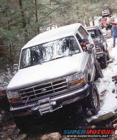 White Ford Bronco with winch on front bumper, driving on snowy, rocky terrain