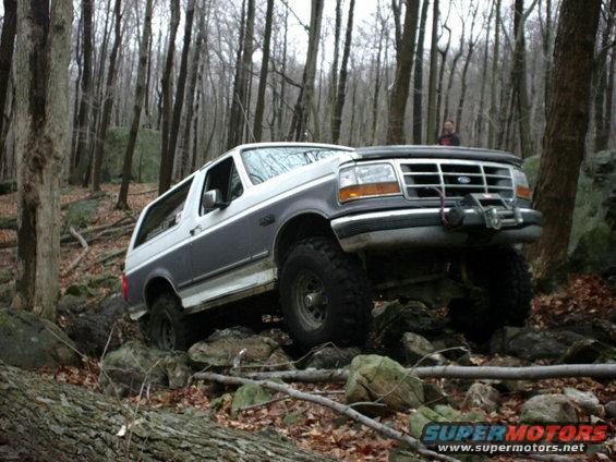1995 Ford Bronco climbing over rocks in a wooded area. Winch is mounted on the front bumper