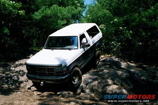1995 Ford Bronco driving over rocks on a wooded trail
