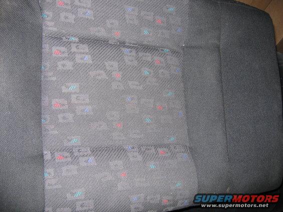 Close-up of gray car seat fabric with a repeating geometric pattern of red, blue, and teal squares