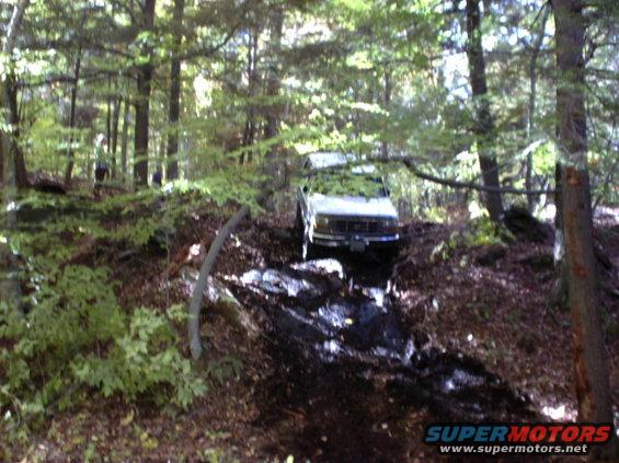 1995 Ford Bronco driving through a wooded area with a muddy path