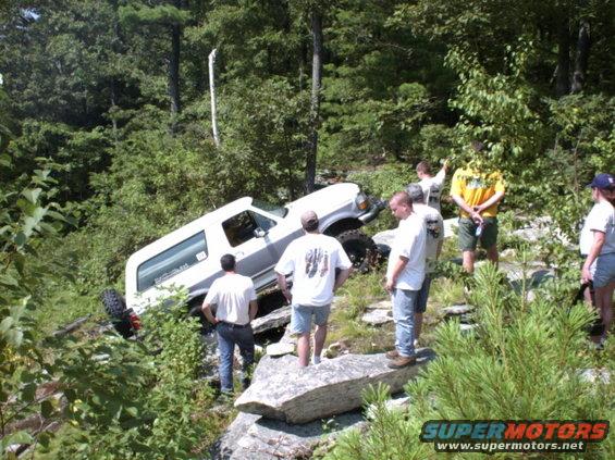 White 1995 Ford Bronco stuck on a rocky incline with people watching