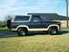 1986 Ford Bronco - A two-tone Ford Bronco is shown parked on a grassy area with a house in the background.