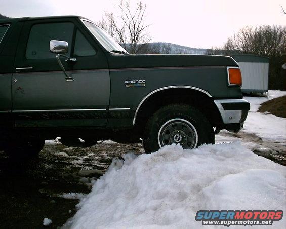 Dark green and gray Ford Bronco partially buried in snow, side view