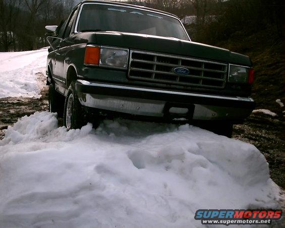 Dark green Ford F-series truck stuck in snow, front view. Grille indicates 1987-1991 model