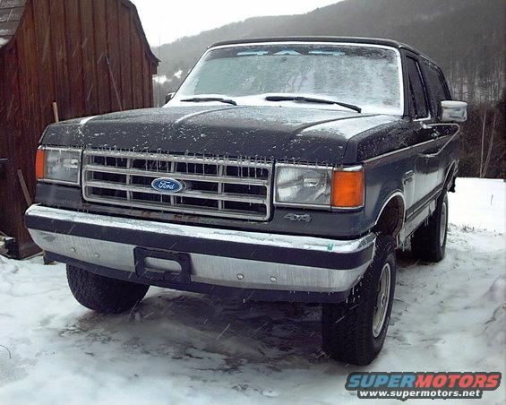 Dark blue Ford Bronco parked in snow, front view. Grille has Ford logo