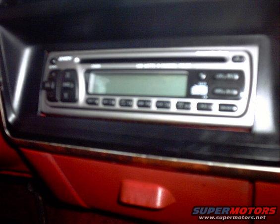 Car stereo with buttons and a digital display, set in red dashboard trim