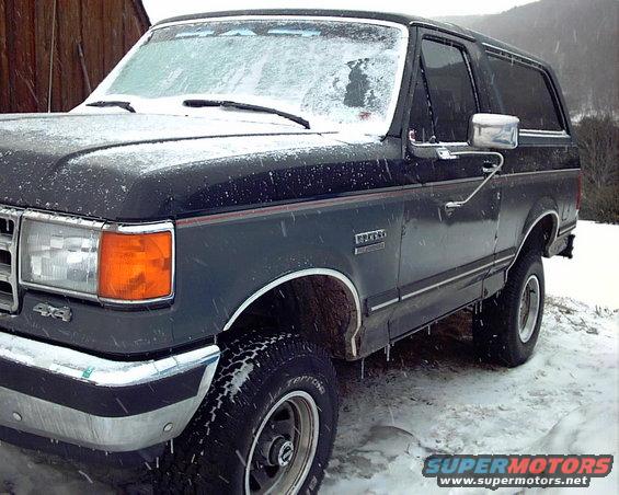Dark gray Ford Bronco with 4x4 badge parked in snow, front quarter view