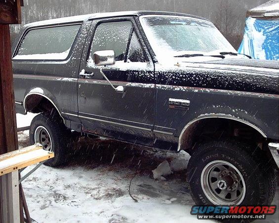 Dark Ford Bronco parked outside in the snow. Side view shows front fender and door