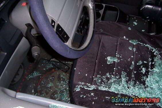Car interior with shattered glass on the seats and floor, steering wheel visible